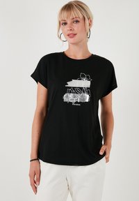 Sort t-shirt med korte ærmer, prydet med et hvidt blomstermotiv og teksten "Floraisson" på forsiden. Blødt stof, afslappet pasform.