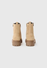 Bottines en suède beige à la finition texturée, dotées d'une fermeture éclair à l'arrière et d'une semelle en caoutchouc épaisse avec un motif de semelle.
