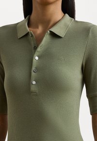 Oliven grønn ribbet polo skjorte med korte ermer, med klassisk krage og fem sølvknapper. Diskret logo på brystet.