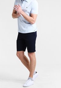 Light blue polo shirt with short sleeves, navy shorts, and white sneakers. The polo features a subtle logo on the chest.
