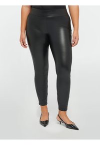 Leggings in ecopelle nera con una texture liscia e lucida e una cintura elastica, aderenti dalla vita fino alle caviglie. Indossati con tacchi neri con borchie.