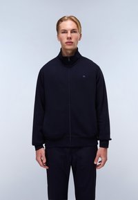Marine zip-up jakke med høy krage, laget av mykt stoff; har ribbestrikkede mansjetter og hem, logo på brystet, og et rent, minimalistisk design.