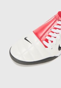 Chaussure de sport blanche et rouge avec une tige texturée et matelassée, logo Nike noir, lacets blancs et semelle en caoutchouc noir.