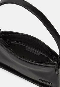 Sac à main en cuir noir avec une texture lisse, une poche zippée à l'intérieur, une longue bandoulière et une forme rectangulaire. Détail de logo en relief notable.