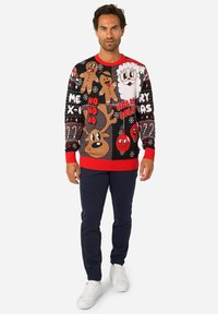 Crni džemper od pletenine s crvenim detaljima, ukrašen svečanim motivima Djeda Mraza, jelena, medenjaka i prazničnim izrekama.