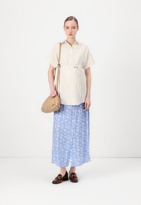 Blusa a righe bianche e crema con maniche corte, cintrata in vita, abbinata a una gonna maxi blu con fiori e mocassini marroni. Borsa beige.