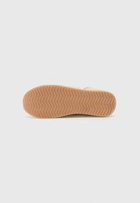 Semelle de chaussure en caoutchouc beige avec un motif de bande de roulement en zigzag, présentant une surface texturée et des bords arrondis pour une meilleure adhérence.