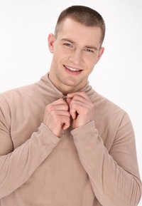 Beige fleece hoodie med halv lynlås krave, blød tekstur, lange ærmer og glat stof. Hænderne griber fat i lynlåsen.