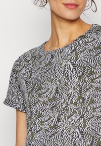 T-shirt de manga curta em verde-oliva com um padrão floral de folhas brancas, gola redonda e um tecido macio e texturizado.