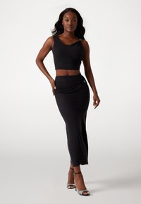Schwarzes Crop-Top mit Rundhalsausschnitt und drapiertem Detail, kombiniert mit einem figurbetonten schwarzen Rock, der einen Seitenschlitz und geraffte Akzente aufweist.