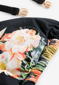 Geantă din material textil negru cu model floral colorat, având un design strâns, accente metalice aurii și curele reglabile.