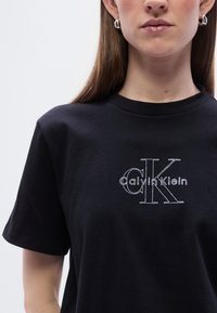 Μαύρο βαμβακερό t-shirt με λευκό κεντητ ό λογότυπο "Calvin Klein", κοντά μανίκια και στρογγυλή λαιμόκοψη. Λείο ύφασμα και κανονική εφαρμογή.