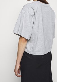 Grå kortärmad t-shirt i mjuk bomull, med avspänt snitt. Slät textur med en enkel design, matchad med en mörk kjol.