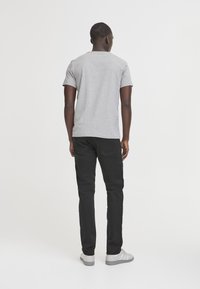 T-shirt grigia in cotone a maniche corte con scollo arrotondato, abbinata a jeans neri slim-fit e sneakers grigie, vista da dietro.