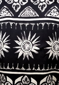 Schwarzer Stoff mit weißen handgezeichneten Mustern, darunter stilisierte Sonnenblumen und geometrische Formen mit filigranen Details und Texturen.