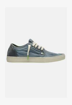 Zapatillas de denim en azul claro con un talón texturizado en azul oscuro. Cuentan con cordones crema y un acento verde cerca del ojal. Suela de goma.