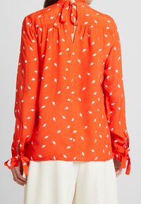 Rode blouse met een bloemenpatroon, lange mouwen, strikjes bij de manchetten en een keyhole rug. Gemaakt van lichtgewicht stof met een gladde textuur.