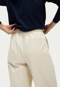 Pantalons beiges à taille élastique avec une poche arrière, associés à un haut bleu foncé à manches longues. Le tissu semble doux avec une texture lisse.