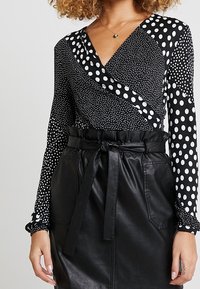 Czarnobiały top w grochy z długim rękawem i kopertowym dekoltem, zestawiony z czarną, wysokowasim spódnicą z imitacji skóry z paskiem.