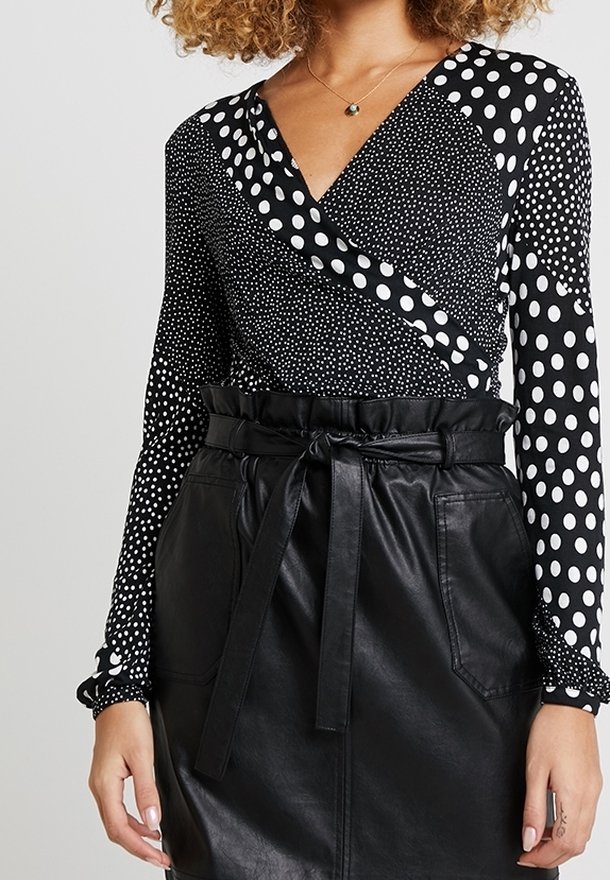 Czarnobiały top w grochy z długim rękawem i kopertowym dekoltem, zestawiony z czarną, wysokowasim spódnicą z imitacji skóry z paskiem.