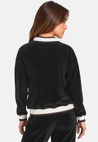 Pullover in velour nero con colletto e polsini a coste bianchi. Presenta una vestibilità comoda e una leggera lucentezza, adatto per un look informale.