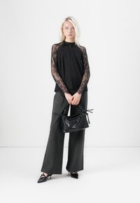 Black top with lace long sleeves, high neckline; gray wide-leg trousers; black textured handbag; pointed black shoes. Minimalist aesthetic.