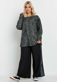 Haut à manches longues imprimé léopard en gris et noir, associé à un pantalon noir ample avec un panneau latéral à motif léopard et des baskets.