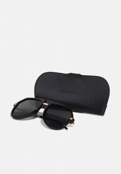 Mustad oktagonaalsed prillid tumedate läätsedega on kaunistatud kuldsete detailidega ning neid hoiab must nahast karp, millel on sisse trampitud tekst "DOLCE & GABBANA."