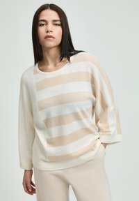 Beige-weißer gestreifter Pullover mit Rundhalsausschnitt und 3/4-Ärmeln aus weichem Material. Das Design weist ein asymmetrisches Streifenmuster auf.