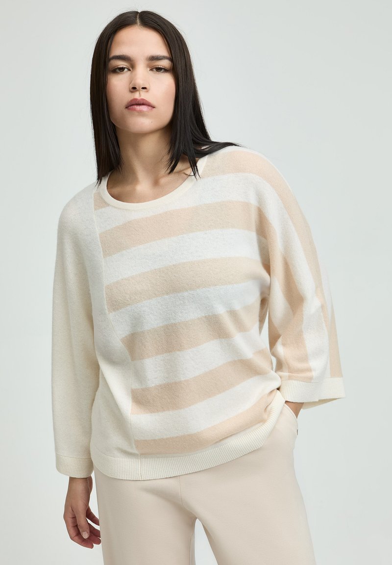 Beige-weißer gestreifter Pullover mit Rundhalsausschnitt und 3/4-Ärmeln aus weichem Material. Das Design weist ein asymmetrisches Streifenmuster auf.