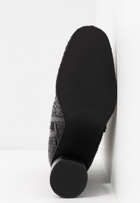 Zapato tejido negro con suela plana, que presenta un empeine texturizado y una suela exterior lisa y de color negro sólido. Talla 37 marcada en la suela.