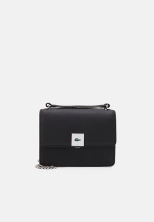 Bolso rectangular negro con asa superior y correa de cadena plateada, con un pequeño cierre cuadrado con un logo de cocodrilo verde.