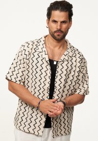 Kurzärmliges Hemd in Beige mit schwarzen Zickzackmustern, aus strukturiertem Stoff, mit Knopfleiste und Kragen.