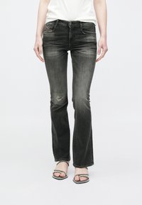 Čierne rozšírené rifle s opotrebovanými detailmi, disponujúce stredne vysokým pásom, klasickým dizajnom s piatimi vreckami a jemným vyblednutím po celej ploche.