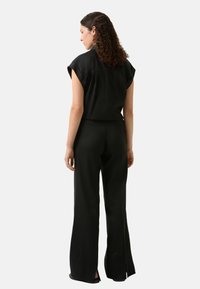 Zwart tweedelig outfit met een shirt met korte mouwen en flared broeken. Het materiaal is gestructureerd, met zijsplitten aan de broekspijpen.