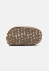 Crocs-sandal med en fluffig �överdel i ljusrosa, med en texturerad gummisula som har "crocs" tryckt i ett upprepat mönster.