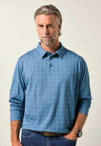Pánská polo košile s dlouhým rukávem v světle modré barvě, s jemným vzorem, se zapínacím límečkem a měkkou texturou. Je spárována s tmavými džíny a hodinkami.