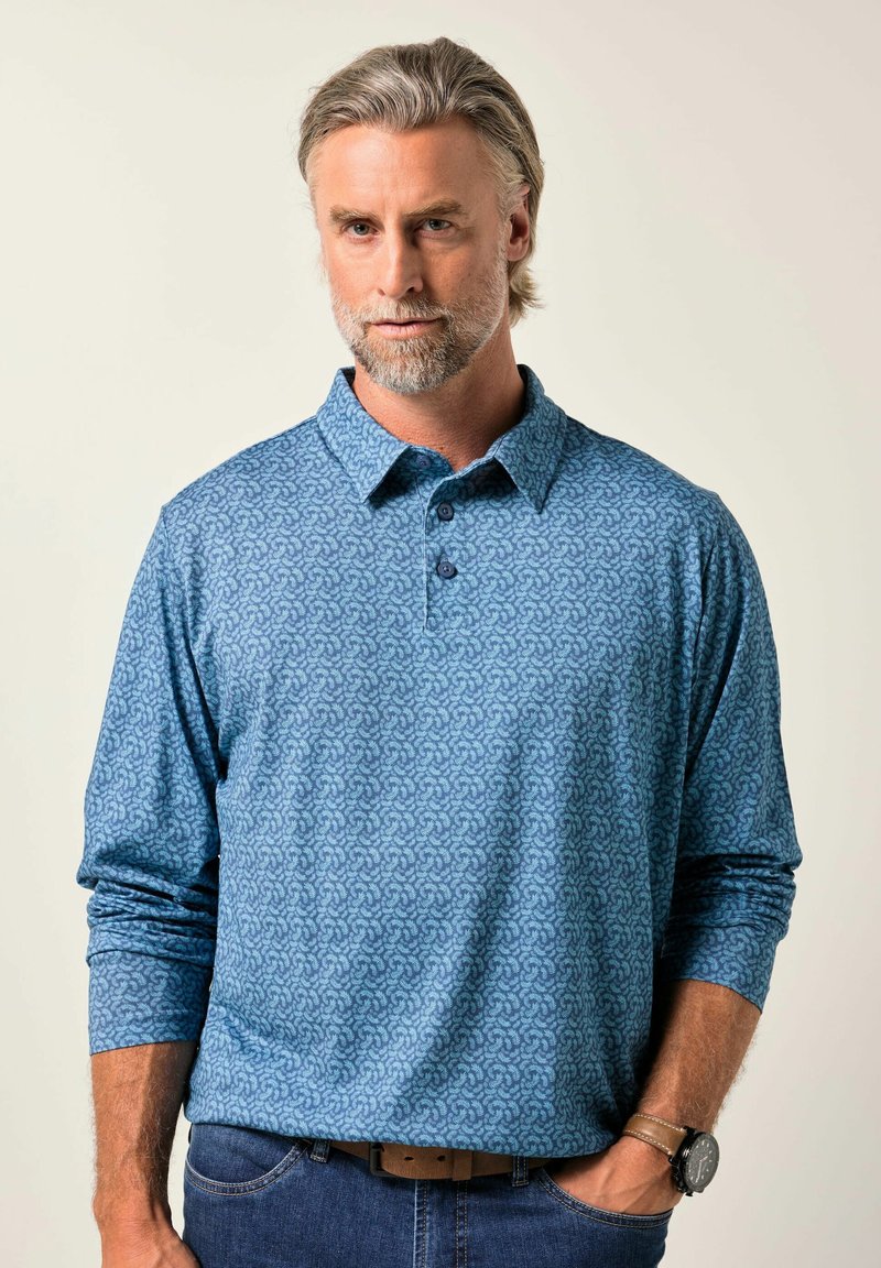 Pánská polo košile s dlouhým rukávem v světle modré barvě, s jemným vzorem, se zapínacím límečkem a měkkou texturou. Je spárována s tmavými džíny a hodinkami.