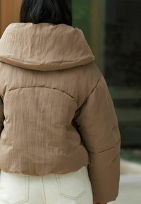 Kohvane puhvjakas, millel on avar kapuuts, tekstuuriga kangas ja lühike disain, kombineeritud heledad, sobiva lõikega püksid.
