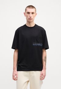 Tricou scurt, negru, din bumbac, cu un buzunar tip patch și logo-ul brodat "HUGO" de culoare albastră pe partea stângă.