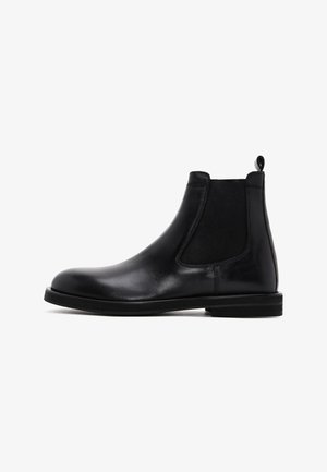Botas Chelsea negras de cuero con paneles laterales elásticos y un tirador. Textura suave, punta redondeada, suela plana de goma.