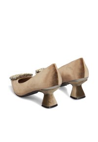 Dei tacchi in suede beige con punta arrotondata, impreziositi da un accento di pietre preziose nella parte anteriore e un design distintivo del tacco a campana.