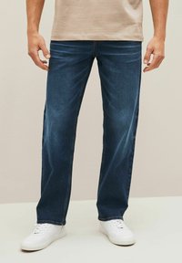 Donkerblauwe denim jeans met een rechte pijp, voorzien van een klassieke vijf-pocket stijl. Gepaard met witte sneakers.