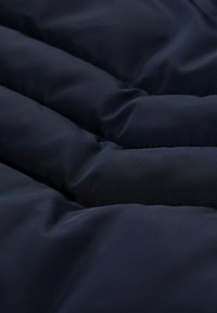 Granatowa, wypełniona tekstylna tkanina o gładkiej powierzchni, z przeszytymi sekcjami zapewniającymi izolację i lekko błyszczącą fakturą.