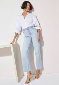 Jeans azzurri a vita alta con gamba dritta, abbinati a una camicia bianca con bottoni e sandali con tacco e straps. Tessuto dalla consistenza morbida.