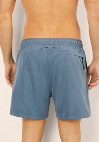 Modré plavkové šortky s elastickým pasem, zadní kapsou na zip a dvěma dekorativními knoflíky vzadu. Jsou vyrobeny z lehkého materiálu.