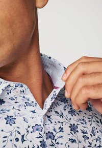 Cămașă albă cu un model floral complex în nuanțe de bleumarin și mov. Dispune de un guler structurat cu căptușeală modelată și o textură netedă.