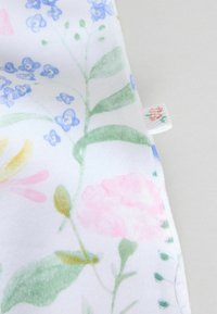 Pehme valge kangas pastelselt lillemustriga roosas, rohelises, sinises ja kollases, millel on lehed ja väikesed lilledetailid.