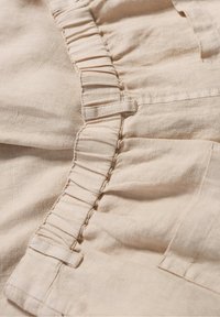 Tissu en lin beige présentant des détails froncés sur le côté, avec une texture lisse et douce et de subtils accents de couture.