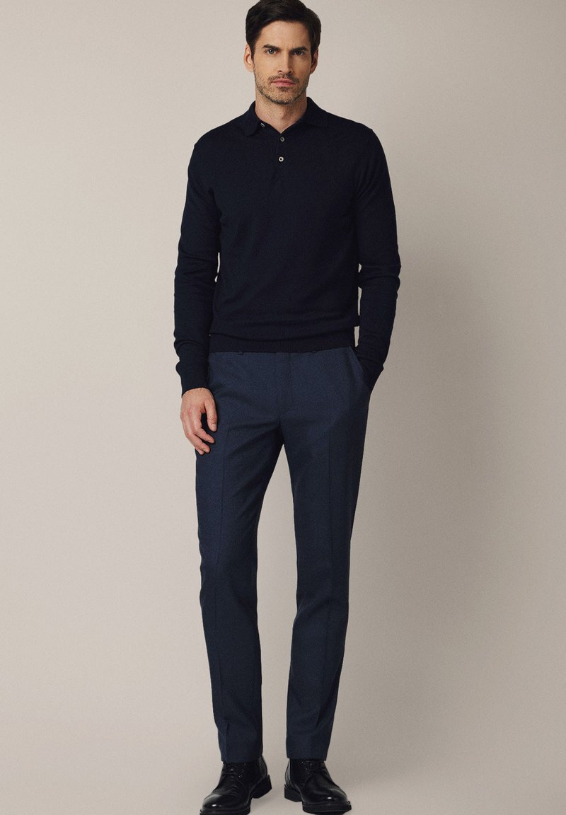 Granatowy dzianinowy sweter polo z kołnierzykiem i dwoma guzikami, połączony z dopasowanymi, ciemnoniebieskimi spodniami, wykończony czarnymi sznurowanymi butami.